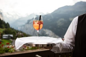 A waiter holding a cocktail on a tray with mountains in the background.