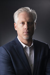 A man in a suit posing for a photo as part of the MegaPlanIT management team.