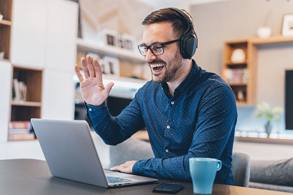 A man with headphones is using a laptop in his living room to ensure cybersecurity and compliance.