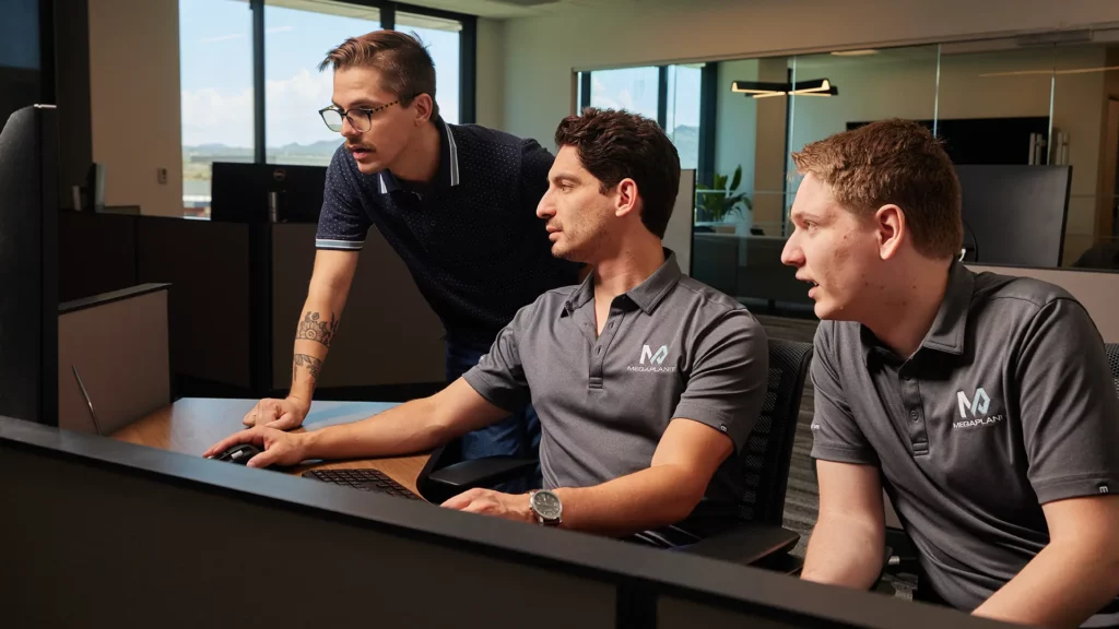 MegaplanIT Security Operation Center Team wearing logo'd polo shirts and looking at one computer screen.